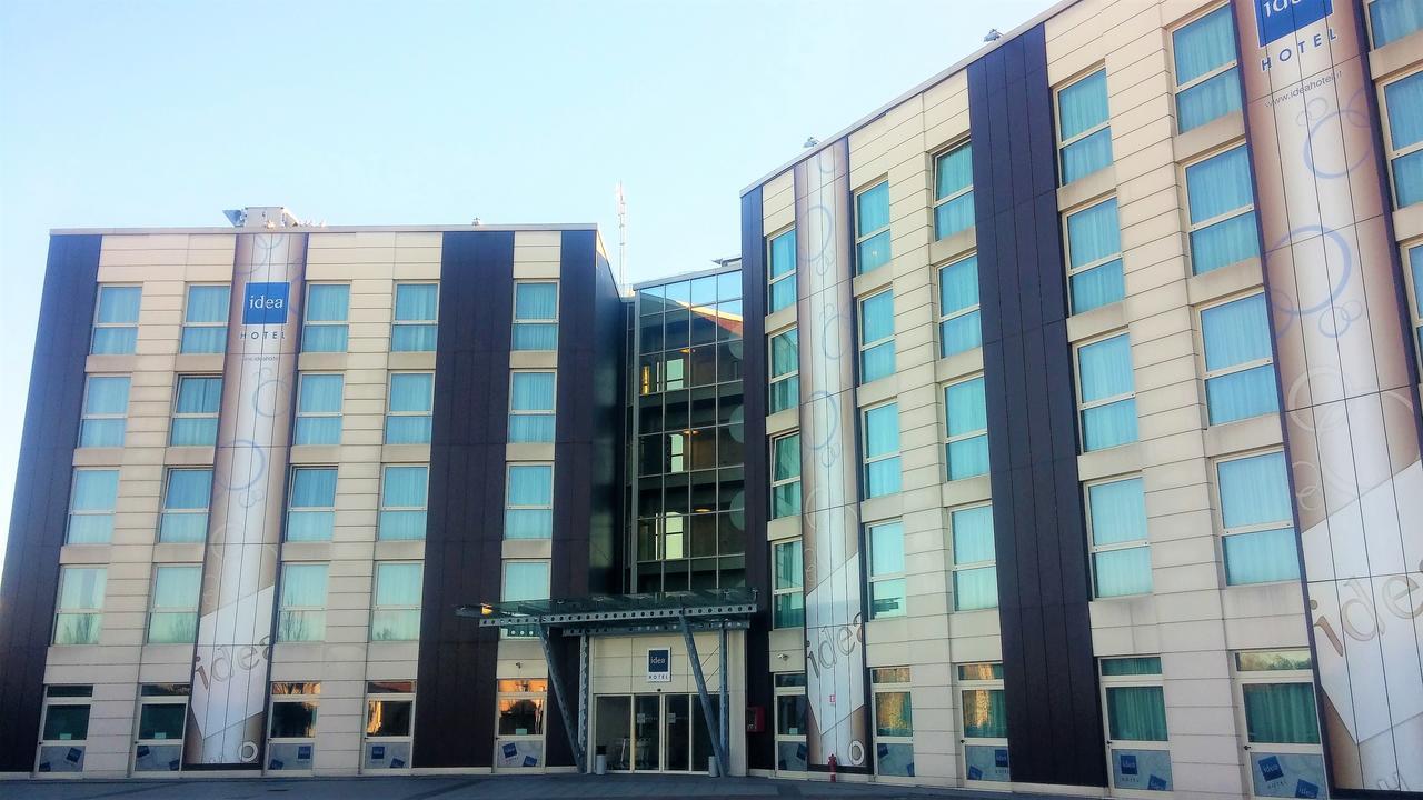 Idea Hotel Milano Malpensa Airport Case Nuove  Esterno foto The photo shows a modern multi-story hotel building. The facade features a combination of light-colored panels and darker accents. There are large windows on each floor, giving the structure a contemporary appearance. The entrance is prominently disp